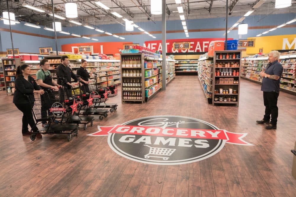 Contestants listen as Host Guy Fieri explains the rules for the Best Fried Dish game, as seen on Guy's Grocery Games, Season 14. (Courtesy, Food Network)