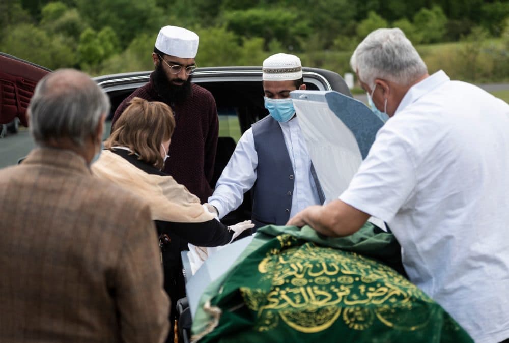 A mourner, wearing a mask and gloves, says her goodbyes after placing dirt in the casket of Ghulam Merzazada at the National Memorial park cemetery in Fairfax, Virginia on May 14, 2020. (ANDREW CABALLERO-REYNOLDS/AFP via Getty Images)