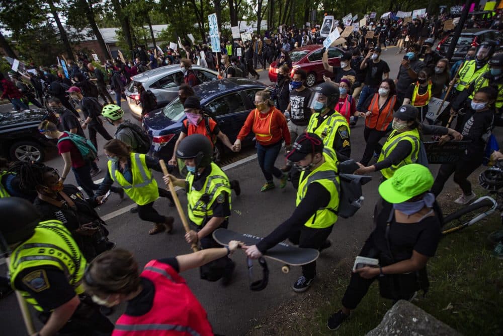 Walking towards Forest Hills Station, protesters wearing vests form a chain around police to keep other protesters from getting near them. (Jesse Costa/WBUR)