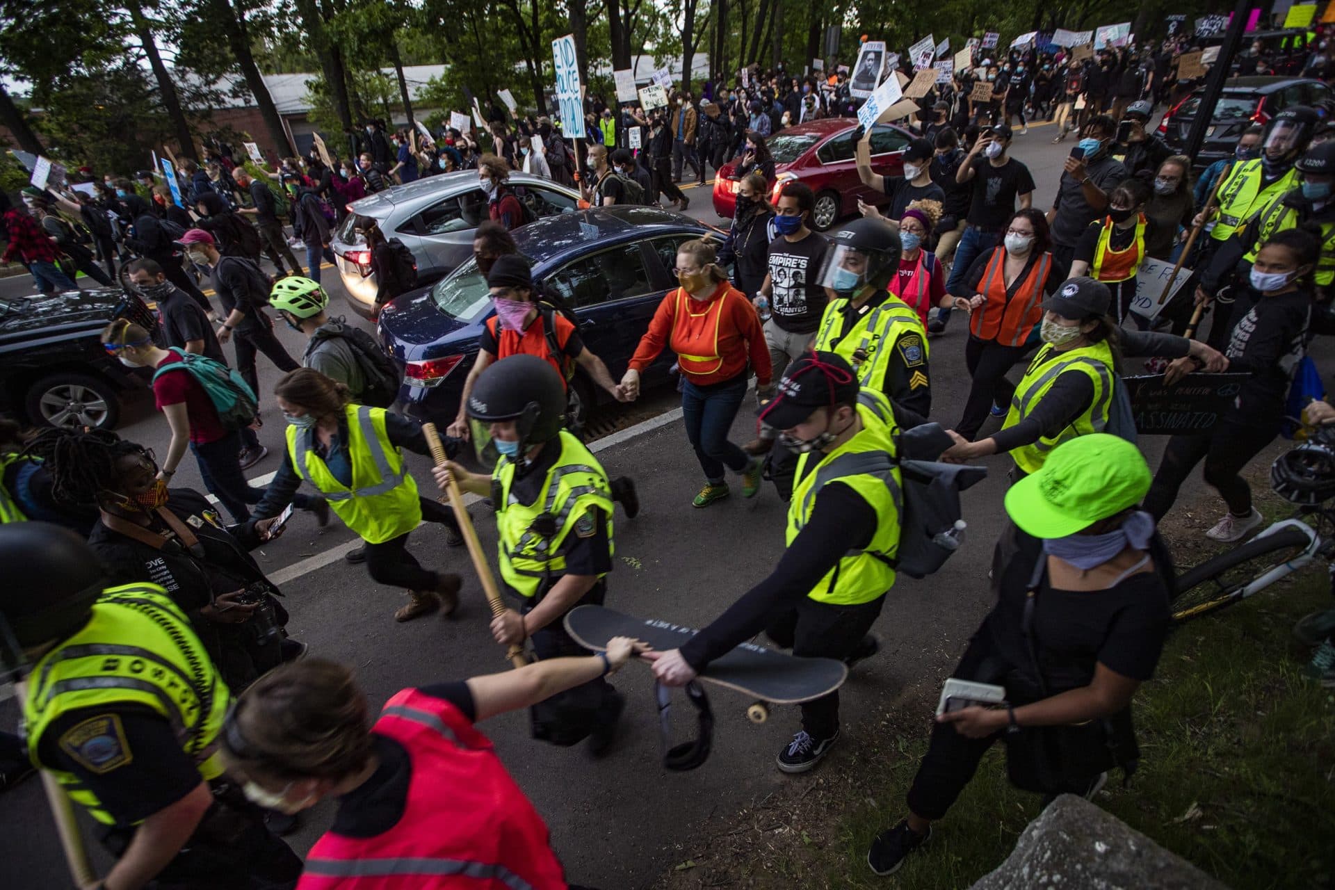 Walking toward Forest Hills Station, protesters wearing vests form a chain around police to keep other protesters from getting near them. (Jesse Costa/WBUR)