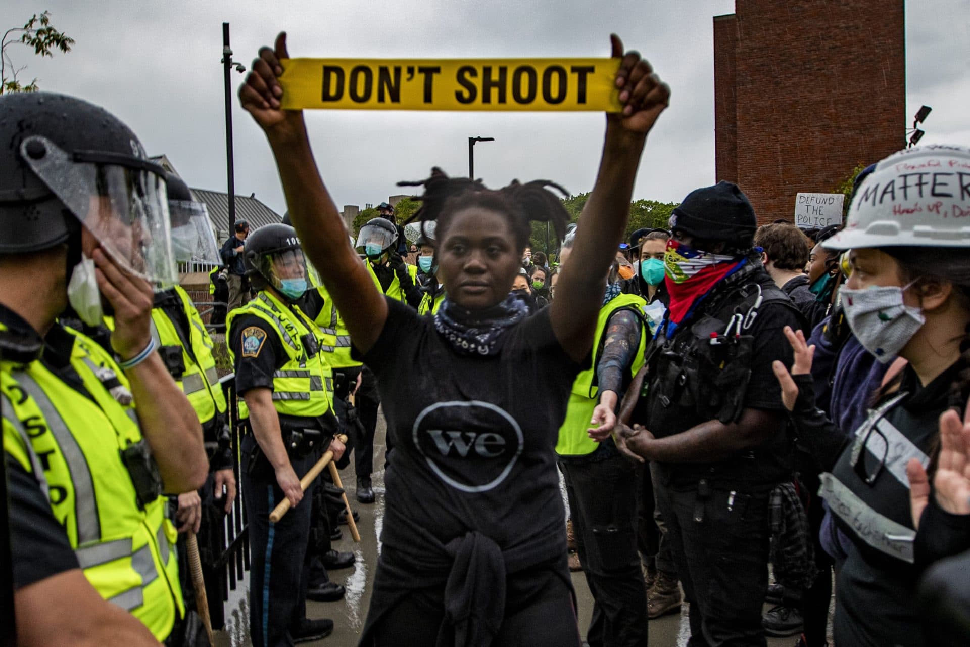 A protester holds up caution tape that reads “don’t shoot” as police and protesters stand off in front of Forest Hills Station in Jamaica Plain. (Jesse Costa/WBUR)
