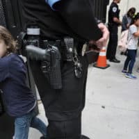 Julian Richner, 9, leaves school for the day to meet his mother as he passes behind an armed security guard at Beverly Hills Unified School District's K-8 Horace Mann School in Beverly Hills, Calif. on Monday, May 13, 2019. Districts nationwide are employing a multi-layered approach for safety that combines mental health programs, bullying prevention initiatives with hardware and software technology, as well as armed and unarmed security officers. (Richard Vogel/AP)