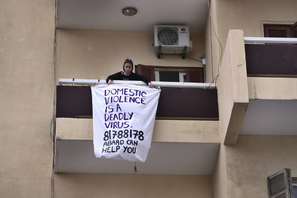 A woman hangs a banner from her balcony with the number of a domestic violence hotline during a national lockdown aimed at stemming the spread of coronavirus, in Beirut, Lebanon, Thursday, April 16, 2020. (Bilal Hussein/AP)