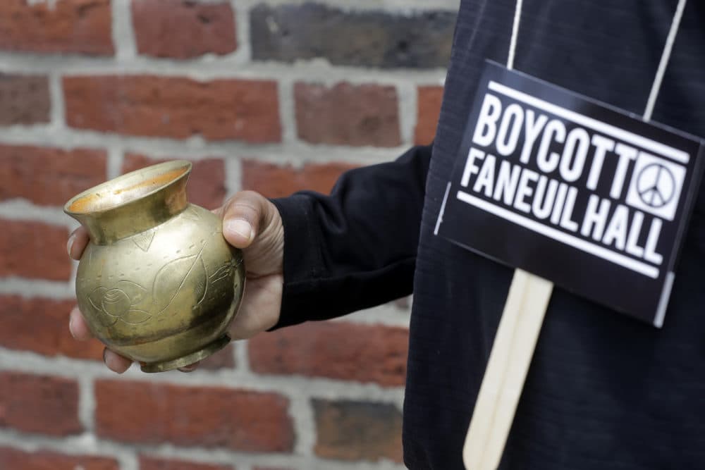 Kevin Peterson, founder and executive director of The New Democracy Coalition pours a red substance as a protest meant to symbolize the blood of fallen black people who died under under white suppression and slavery. Peterson advocates changing the name of Faneuil Hall, as its namesake Peter Faneuil, was a slave owner. (Steven Senne/AP)
