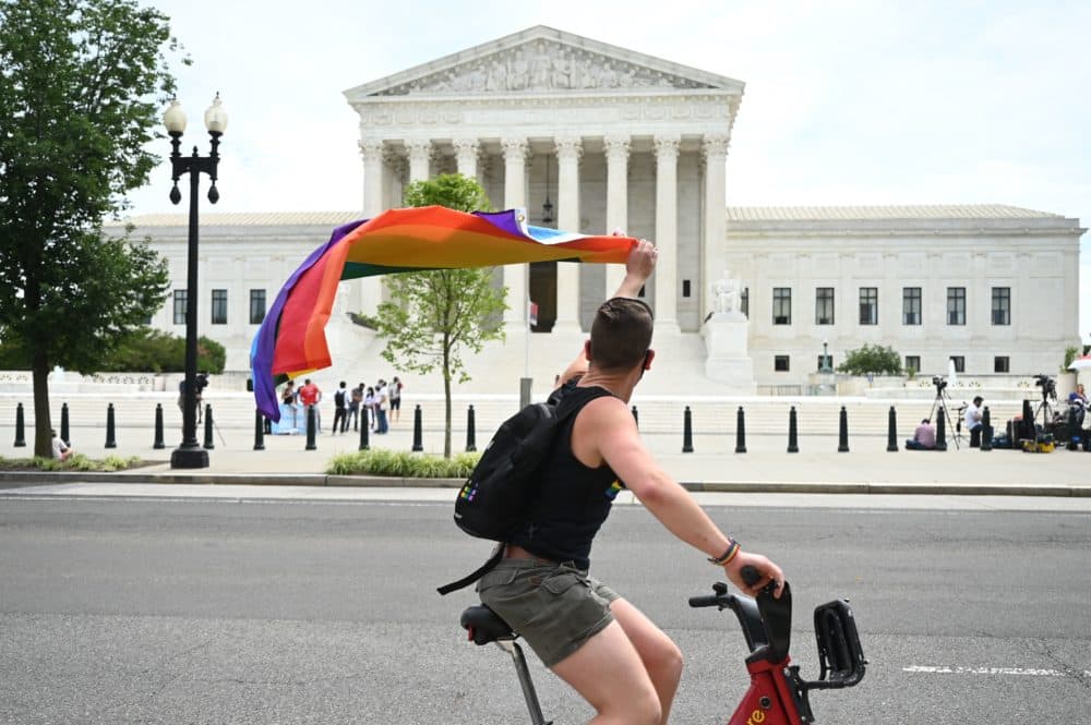 A man waves a rainbow flag as he rides by the US Supreme Court that released a decision that says federal law protects LGBTQ workers from discrimination on June 15, 2020 in Washington,DC. (JIM WATSON/AFP via Getty Images)