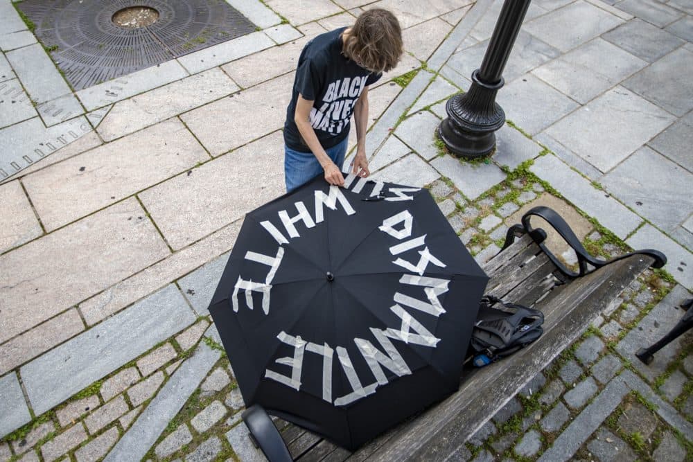 A protester applies white tape on an umbrella spelling out the words “Dismantle White Supremacy” before the march. (Jesse Costa/WBUR)