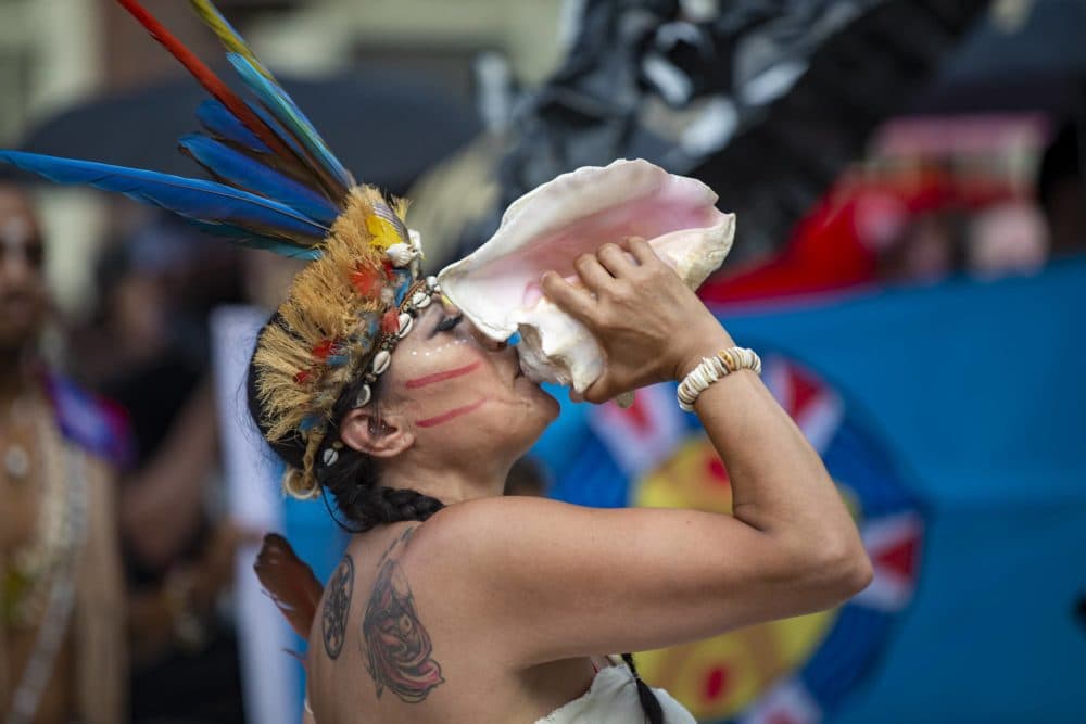 Chali’Naru Dones, of the United Confederation of Taino People, blows through a conch to signal the beginning of the march to Boston City Hall. (Jesse Costa/WBUR)