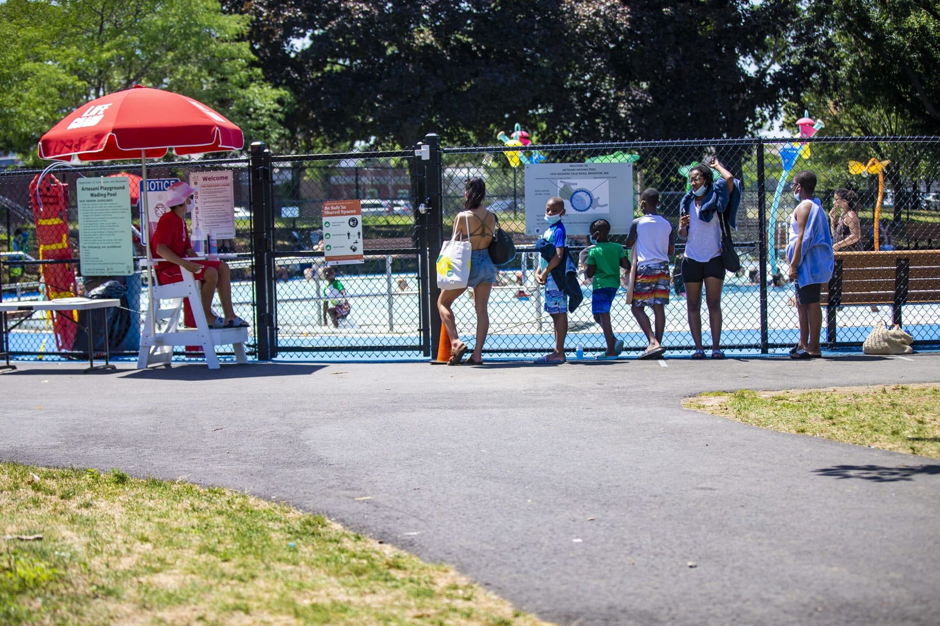 People wait in line to enter the pool at the Artesani Playgound in Allston. The pool is operating at 50% capacity and with special safety precautions for COVID-19. (Jesse Costa/WBUR)