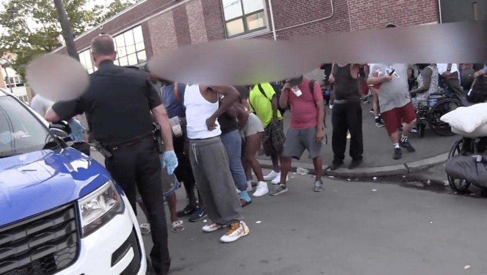 People lined up outside a Boston police cruiser prepare to hand over their IDs so police can run them through the warrant check system during last year's "Operation Clean Sweep." (Boston police footage courtesy ACLU)