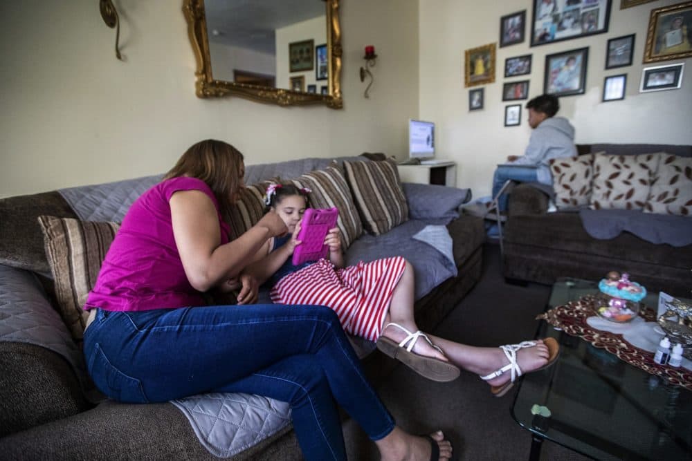 Maragareth Jesus helps her daughter, Luz, on a tablet while her son, Jesus, attends his online class. (Jesse Costa/WBUR)
