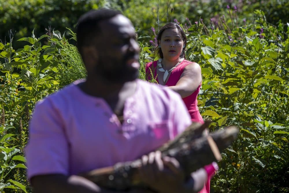 Paige Clark as Miranda peers from behind a bush at Omar Robinson as Ferdinand as they rehearse the log scene in "The Tempest" at the Arnold Arboretum. (Jesse Costa/WBUR)