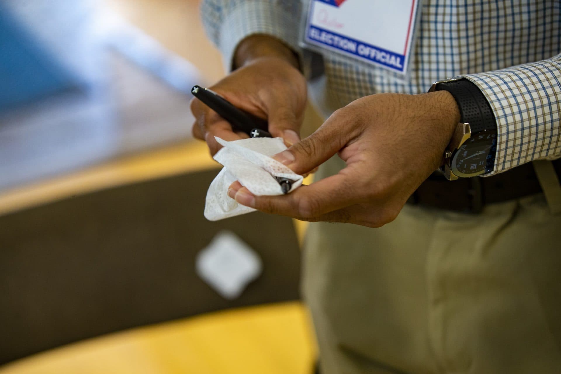 A poll worker disinfects pens used by voters to mark their ballots at Brookline High School. (Jesse Costa/WBUR)