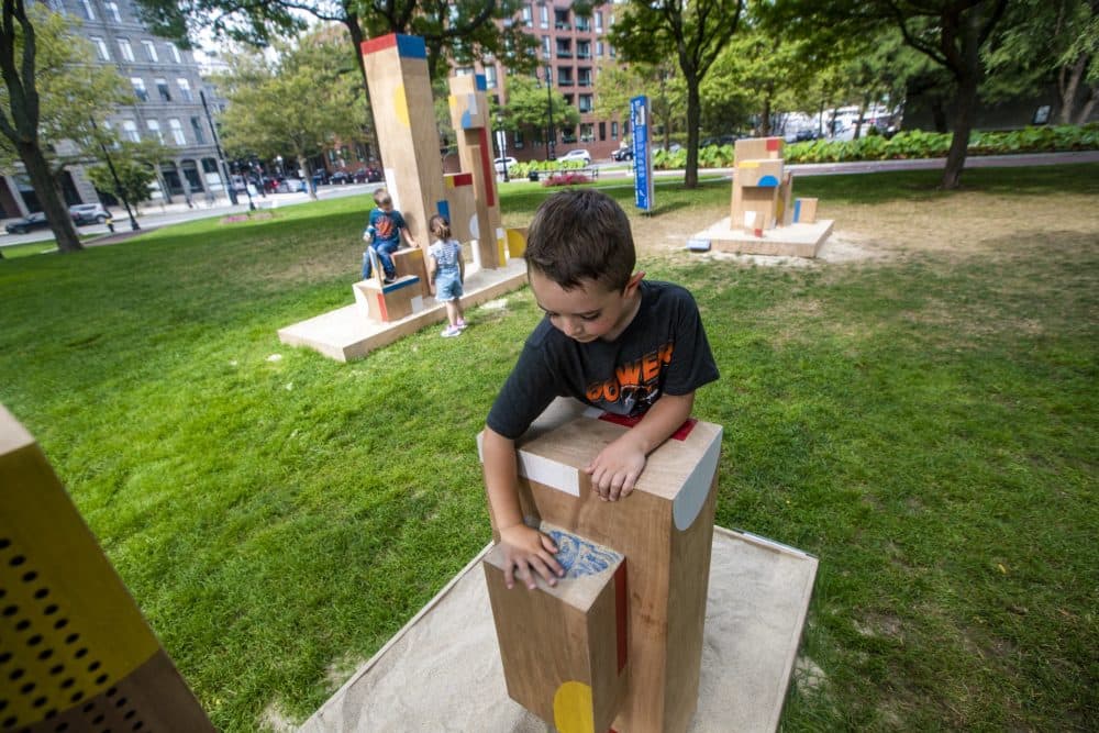 Five-year-old Lucas Bullerous brushes sand off of one of the structures. (Jesse Costa/WBUR)
