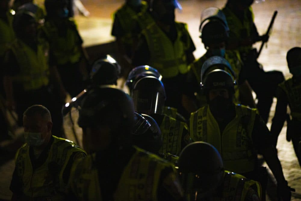 Boston Police officers armed with batons and wearing riot gear climb the stairs of City Hall Plaza on Congress Street as protesters gather on Congress Street during the Justice for Breonna Taylor rally. (Jesse Costa/WBUR)