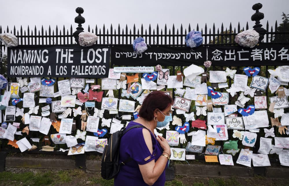 In this May 28, 2020, file photo, a woman passes a fence outside Brooklyn's Green-Wood Cemetery adorned with tributes to victims of COVID-19 in New York. The U.S. death toll from the coronavirus topped 200,000 Tuesday, Sept. 22, a figure unimaginable eight months ago when the scourge first reached the world’s richest nation with its sparkling laboratories, top-flight scientists and towering stockpiles of medicines and emergency supplies. (Mark Lennihan/AP Photo File)