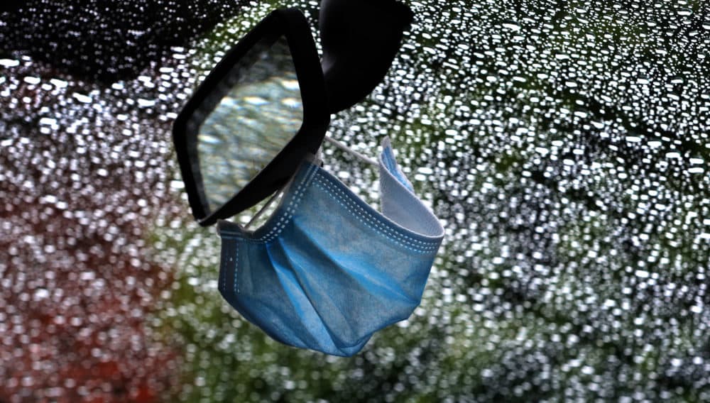 A surgical mask hangs from the rear view mirror of a car parked in the rain.(Karl-Josef Hildenbrand/Getty Images)