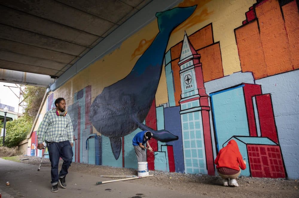 Student artists Brennan Commisso and Delila Montañez work with Jason Talbot, left, on a cityscape and ocean wildlife mural on the East Boston Greenway. (Robin Lubbock/WBUR)