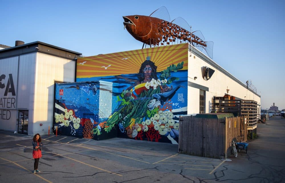 Artist Silvia López Chavez by her mural "Rise" at the Boston Harbor Shipyard and Marina in East Boston. (Robin Lubbock/WBUR)