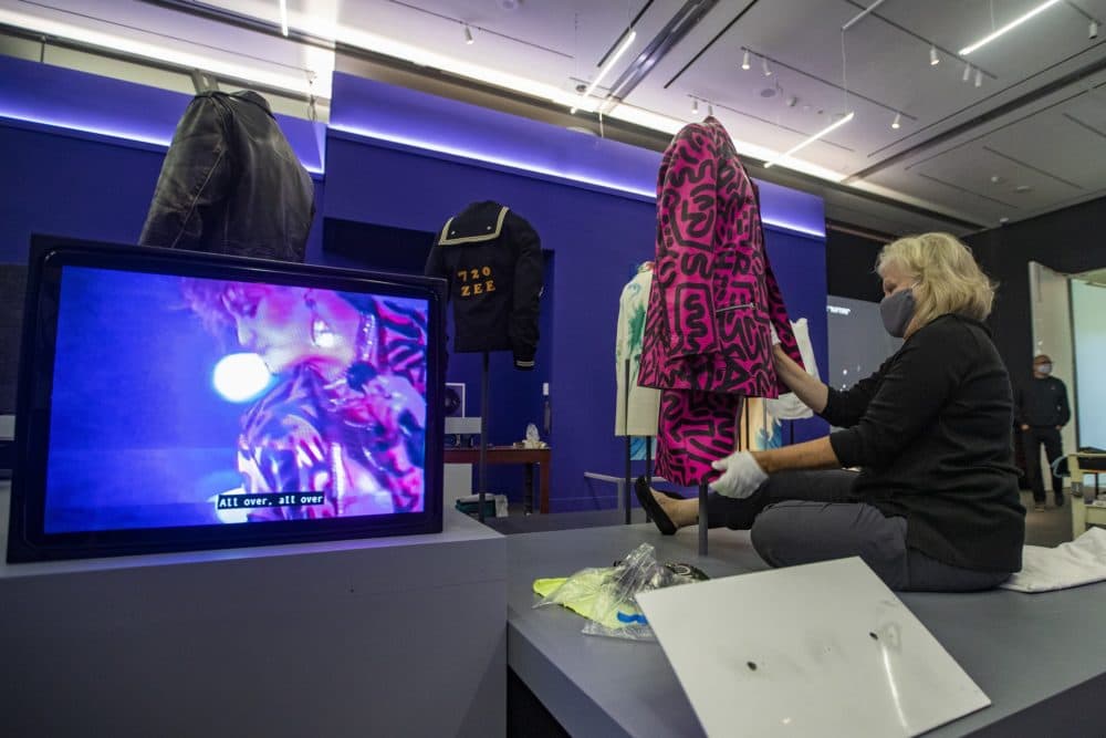 Meredith Montague, head of textile conservation at the Museum of Fine Arts, Boston, installs "Decorated Suit" by Keith Haring and LA2 which was worn by Madonna in 1984, as shown on the video screen. (Jesse Costa/WBUR)