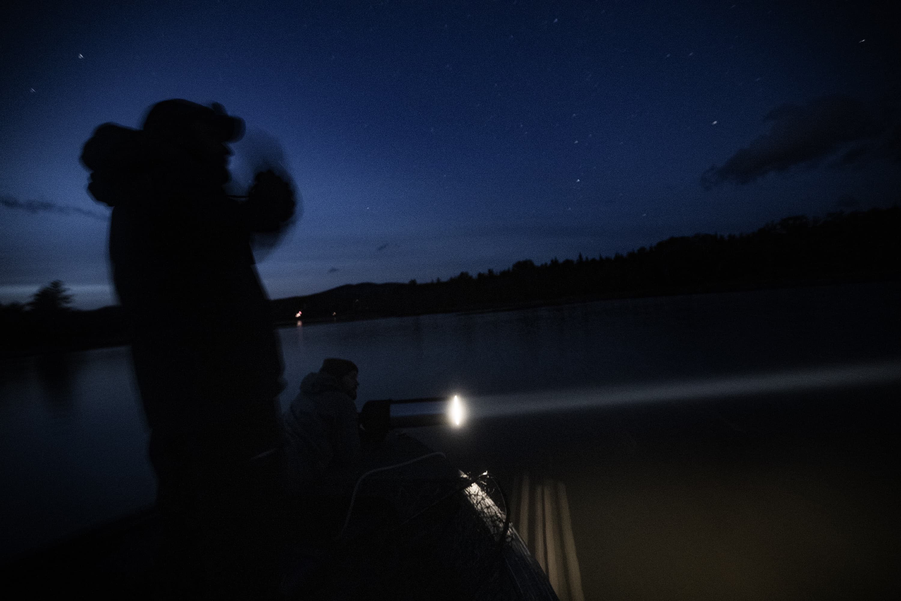 Mark Burton shines a spotlight across the water as Chris Persico uses a pair of binoculars to find loon chicks on Rangeley Lake in Maine. (Jesse Costa/WBUR)