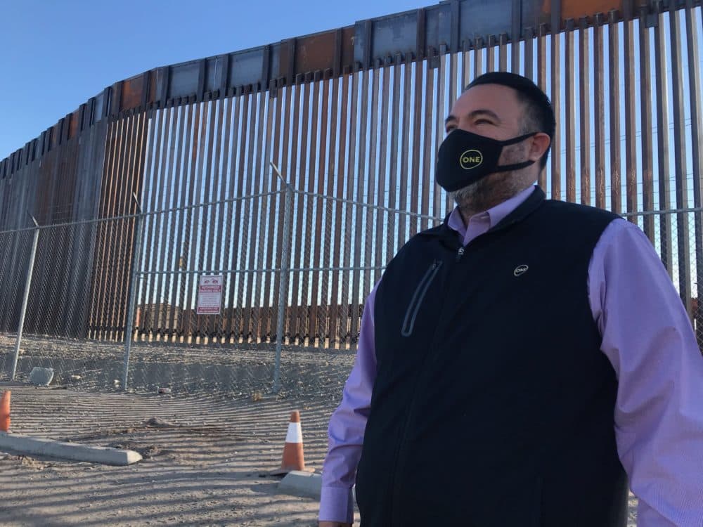 Matias Rosales, vice mayor of San Luis, Arizona, stands in the shadow of a new section of President Trump's border wall. (Peter O'Dowd/Here & Now)