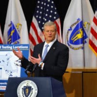 Gov. Charlie Baker stands next to a sign reading "Stop the Spread Testing Locations" as he speaks during a press conference in the Gardner Auditorium in the State House in Boston on Dec. 7. (Pat Greenhouse/The Boston Globe via Getty Images)