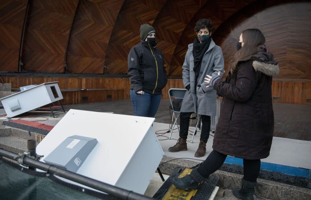Project manager Jane Long, technical director Pamela Hersch and artist Maria Finkelmeier stand by one of the projector boxes that will light up the Hatch Shell for "Hatched: Breaking through the Silence." (Robin Lubbock/WBUR)