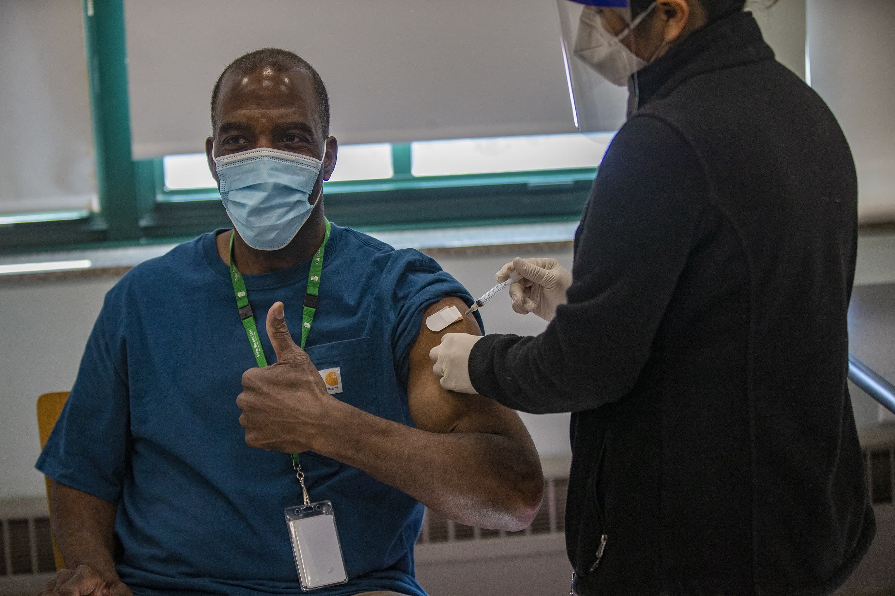 Michael Robbins, a Pine Street Inn counselor for 40 years, is the first to receive a COVID-19 vaccine at the shelter's vaccination event. BHCHP registered nurse Carmen Sargent is administering the shot. (Jesse Costa/WBUR)