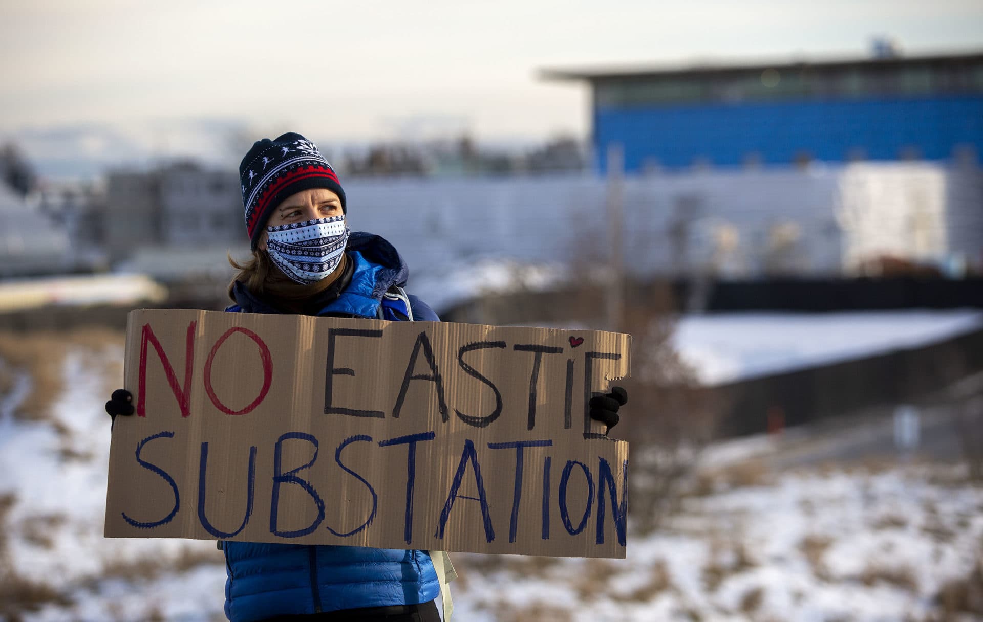 Juliane Manitz carries a "No Eastie Substation" sign at the Extinction Rebellion protest at the Condor Street Urban Wild against the proposed East Boston electrical substation. The proposed site is the fenced, snow covered area behind her. (Robin Lubbock/WBUR)