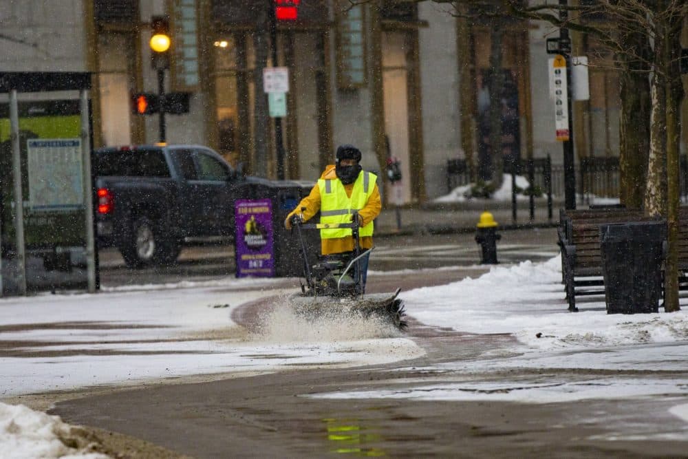 un muncitor curăță zăpada de pe trotuarul din afara Bisericii Trinity din Copley Square luni după-amiază, când începe furtuna. (Jesse Costa / WBUR) 