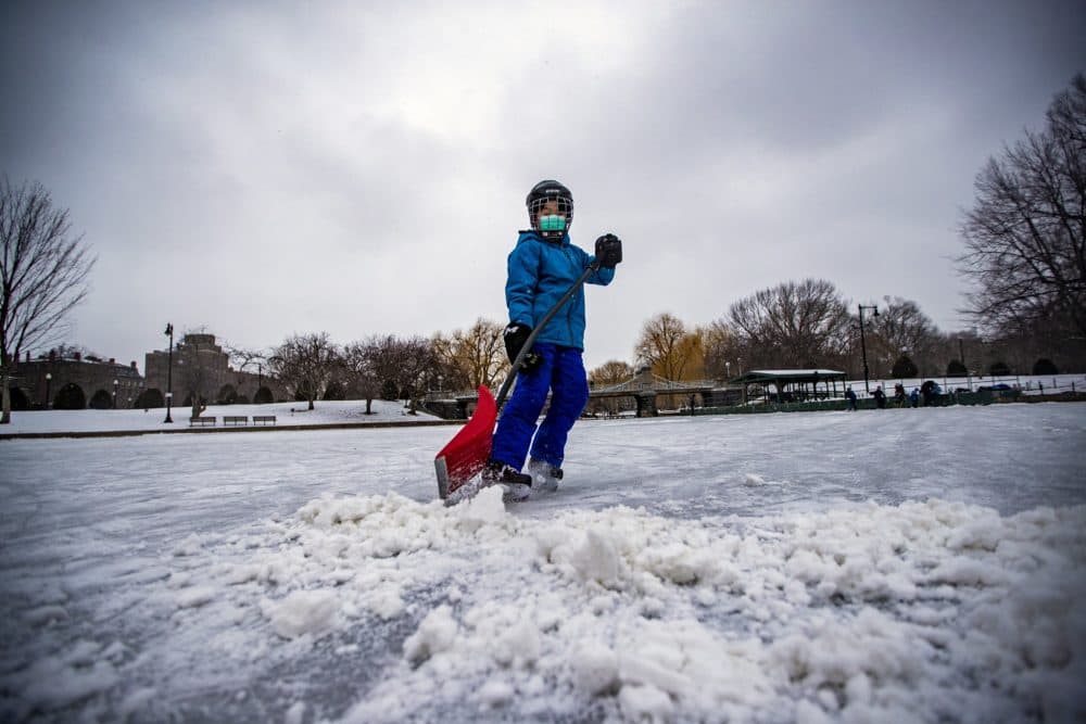  Tanner Li enlève la neige de la glace de l'étang du jardin public de Boston lundi après-midi pour un match de hockey avec ses amis. (Jesse Costa / WBUR) 