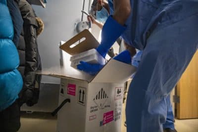 A pharmacy technical worker at Boston Medical Center removes two trays of Pfizer's COVID-19 vaccine, each containing 975 doses, from a box. They will be placed into a freezer kept at a temperature between -60° and -80°. (Jesse Costa/WBUR)