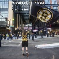 A man waves a Bruins flag on Causeway Street, in front of the entrance of TD Garden before the Bruins/Islanders game, the first game open to the public now that stadiums and arenas are permitted to hold up to 12% capacity since they were restricted by COVID-19 protocols. (Jesse Costa/WBUR)