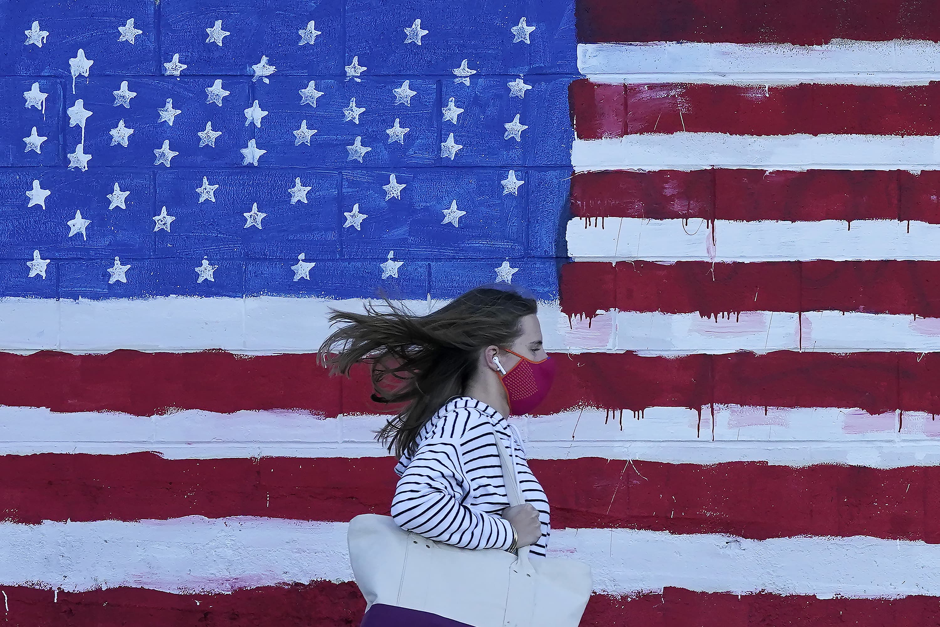 A woman wears a mask while walking past a U.S. flag painted on a wall during the pandemic in San Francisco on Nov. 16, 2020. (Jeff Chiu/AP)