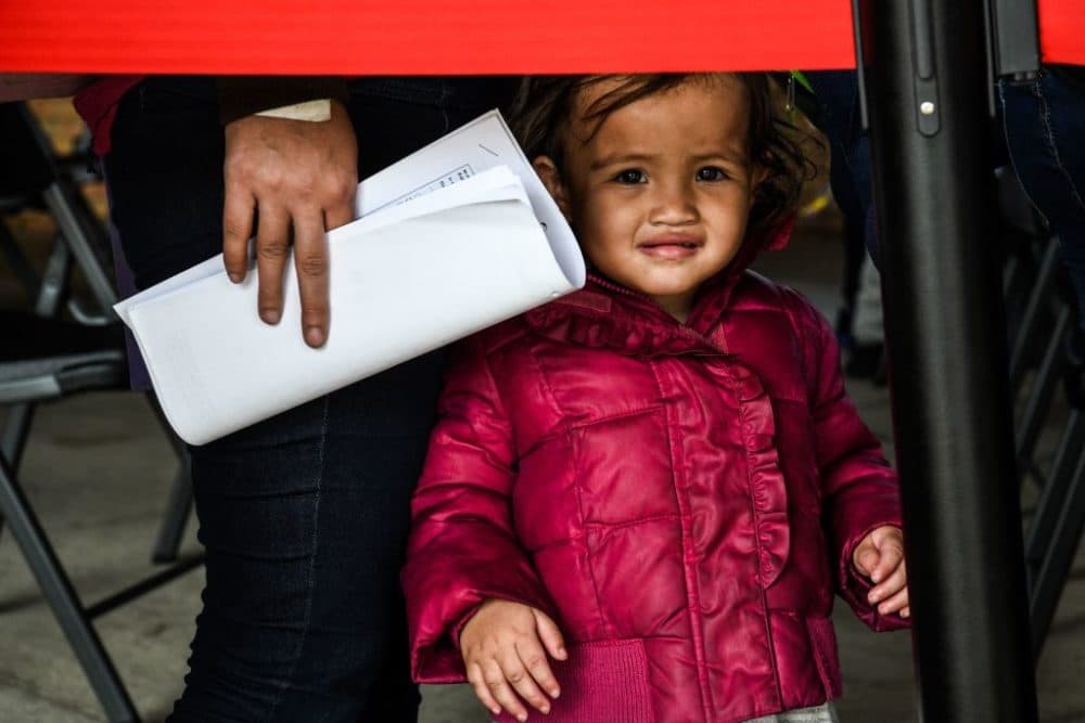 A migrant girl from Central America waits with her mother for a bus after they are dropped off by the US Customs and Border Protection at a bus station near the Gateway International Bridge, between the cities of Brownsville, Texas, and Matamoros, Mexico, on March 15, 2021 in Brownsville, Texas. (Chandian Khanna/AFP via Getty Images)