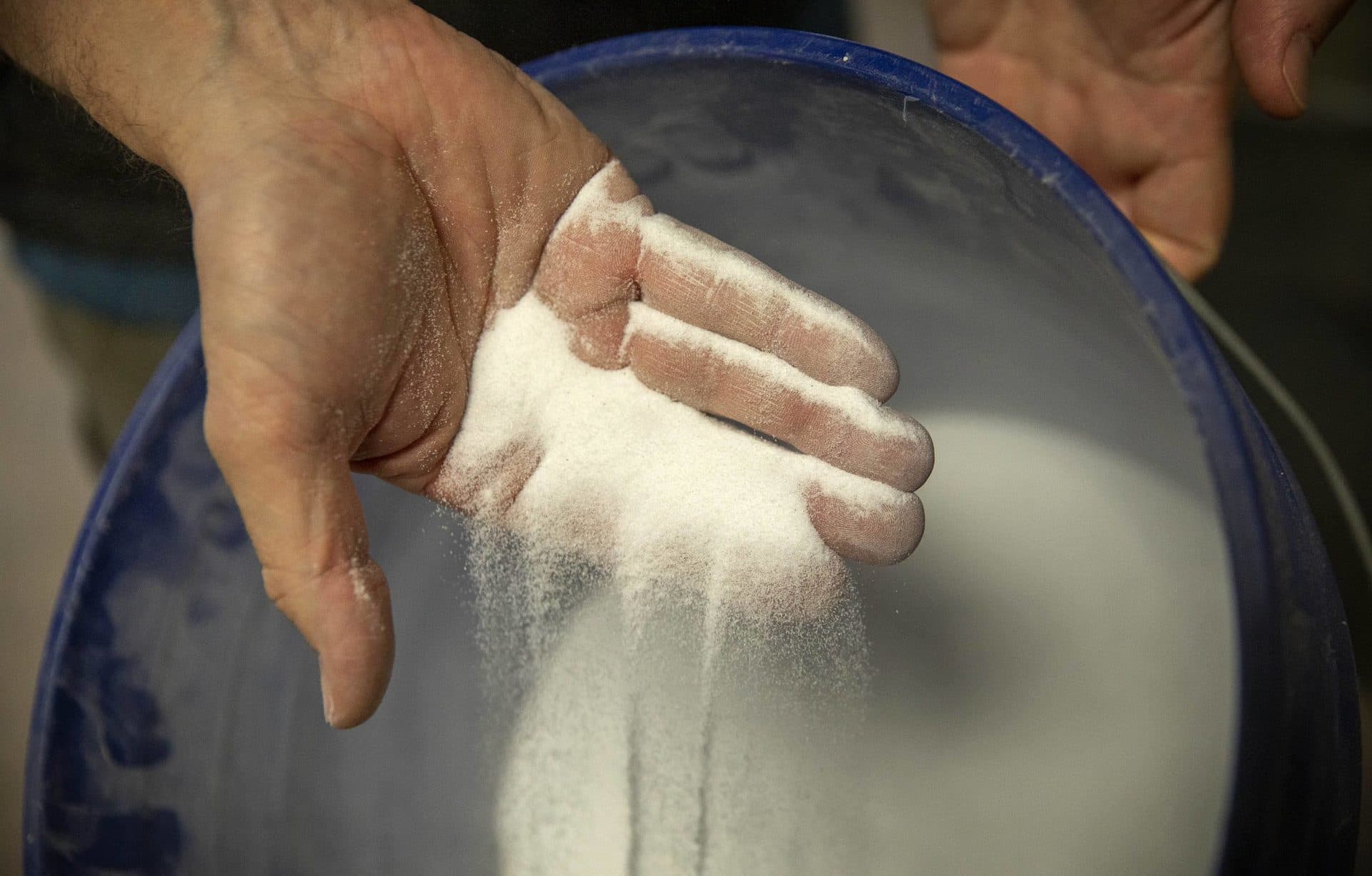Dan Gessler pours a handful of the fine synthetic sediment, designed to work at the model's scale, back into a bucket. (Robin Lubbock/WBUR)