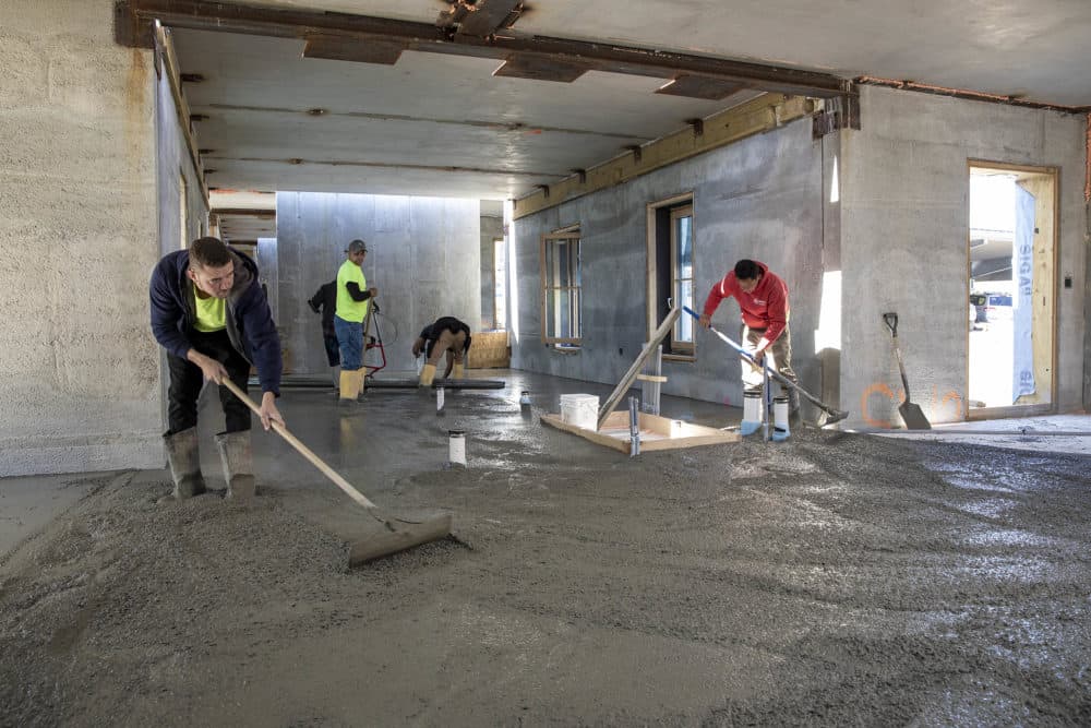 Construction workers spread concrete over a thick layer of insulation to form the ground floor of one of the new passive house buildings at the Hillside Center for Sustainable Living in Newburyport. (Robin Lubbock/WBUR)