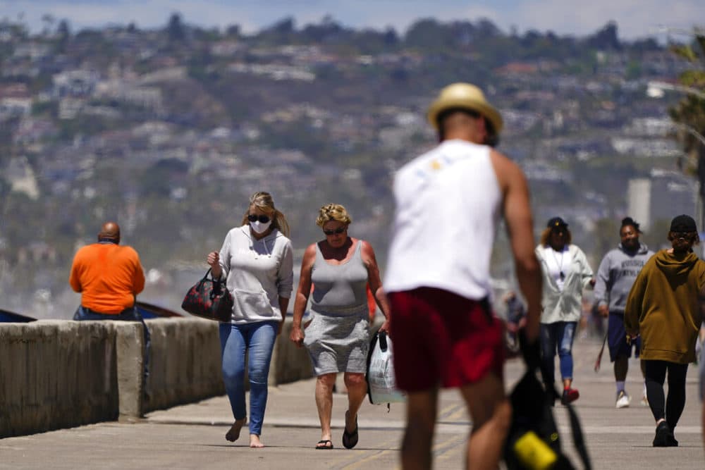 Jean Bourbonnais, left, wears a mask as she walks with Sheryl Nieman Hancock along a beach promenade Tuesday, April 27, 2021, in San Diego. Nieman Hancock is already vaccinated, and Bourbonnais plans to get her vaccine soon. U.S. health officials say fully vaccinated Americans don't need to wear masks outdoors anymore unless they are in a big crowd of strangers. And unvaccinated people can drop face coverings in some cases, too. (AP Photo/Gregory Bull)