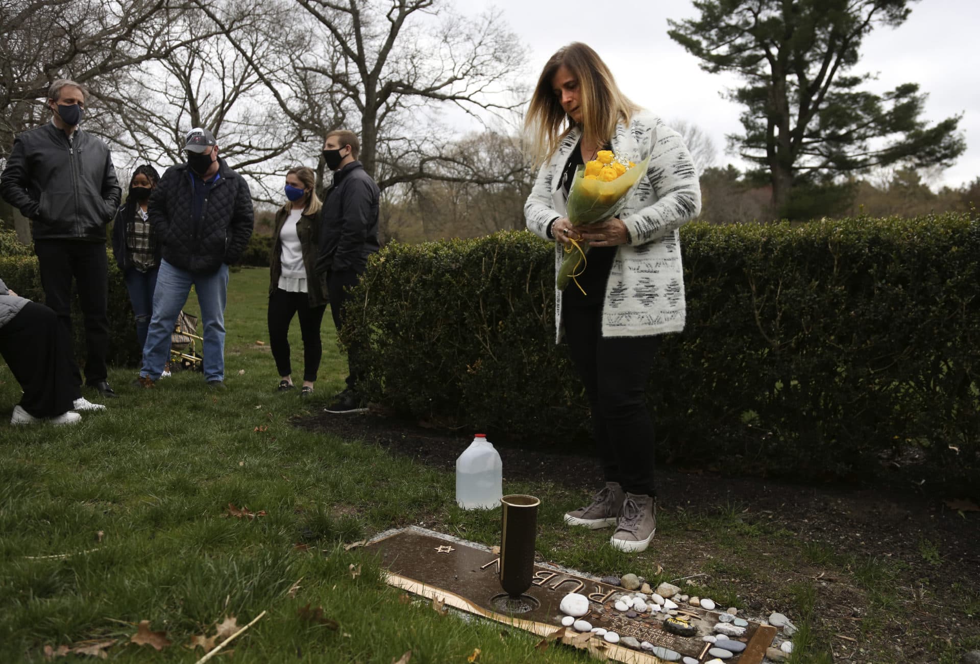 Michelle Pepe places a bouquet of yellow roses on her father's grave as family and friends watch in Sharon, Mass., on Tuesday, April 13, 2021. (Jessie Wardarski/AP)