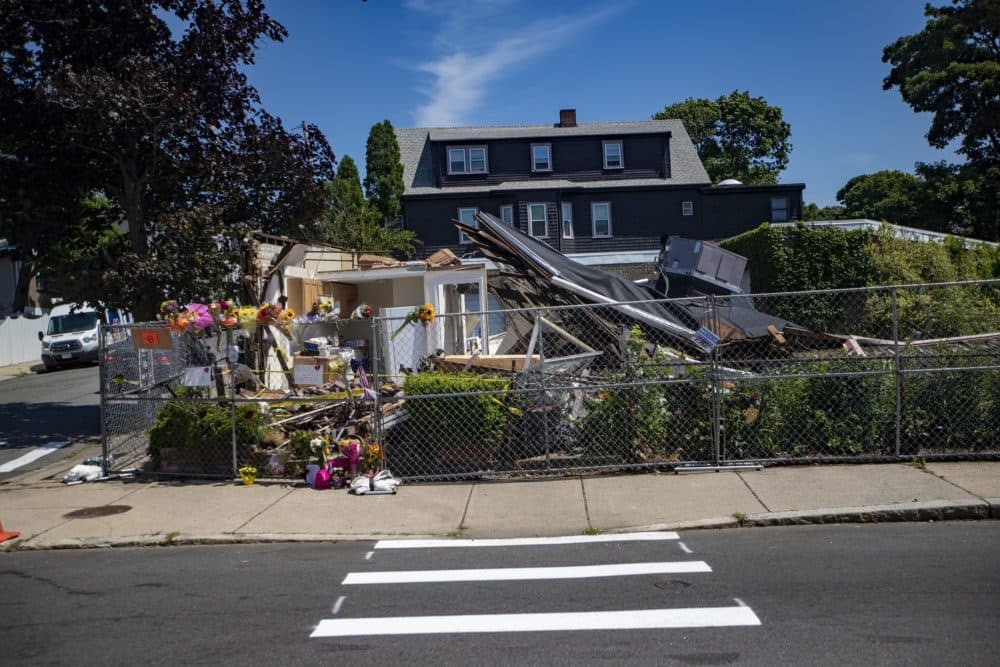 Flowers are seen left outside a fence surrounding a building that was destroyed, authorities say, by the driver of a stolen plumbing company truck. The suspect then shot and killed U.S. Air Force veteran Ramona Cooper and retired Massachusetts State Police trooper David Green. (Jesse Costa/WBUR)