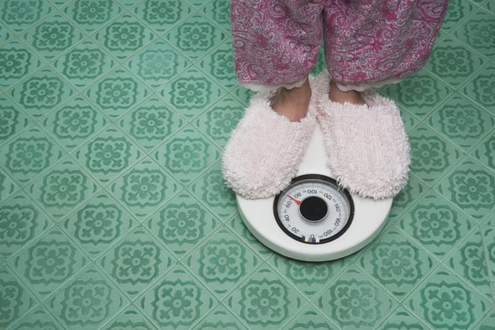 Close up of feet in slippers on bathroom scale. (Getty Images)