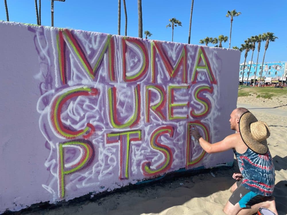 Andrew Patalano spray paints "MDMA cures PTSD" on May 22, 2021, in Venice Beach, California. (Tonya Mosley/Here & Now)