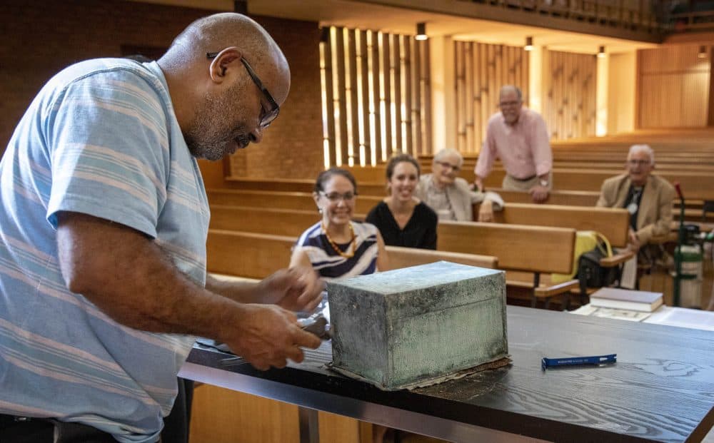 William Valentín pries open the seal of the 1898 copper box found under a cornerstone of the Villa Victoria Center for the Arts, formerly a Lutheran church, when the building was demolished in 2020. (Robin Lubbock/WBUR)