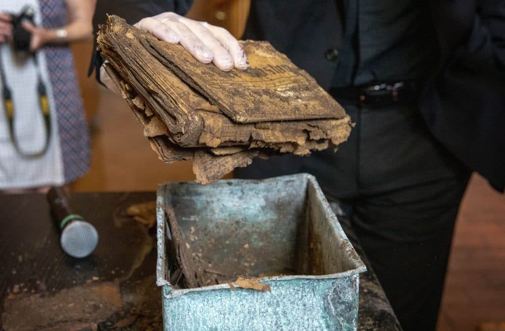 Wearing a protective glove, Rev. James Hopkins gently lifts a bundle of papers from the 1898 copper box. (Robin Lubbock/WBUR)