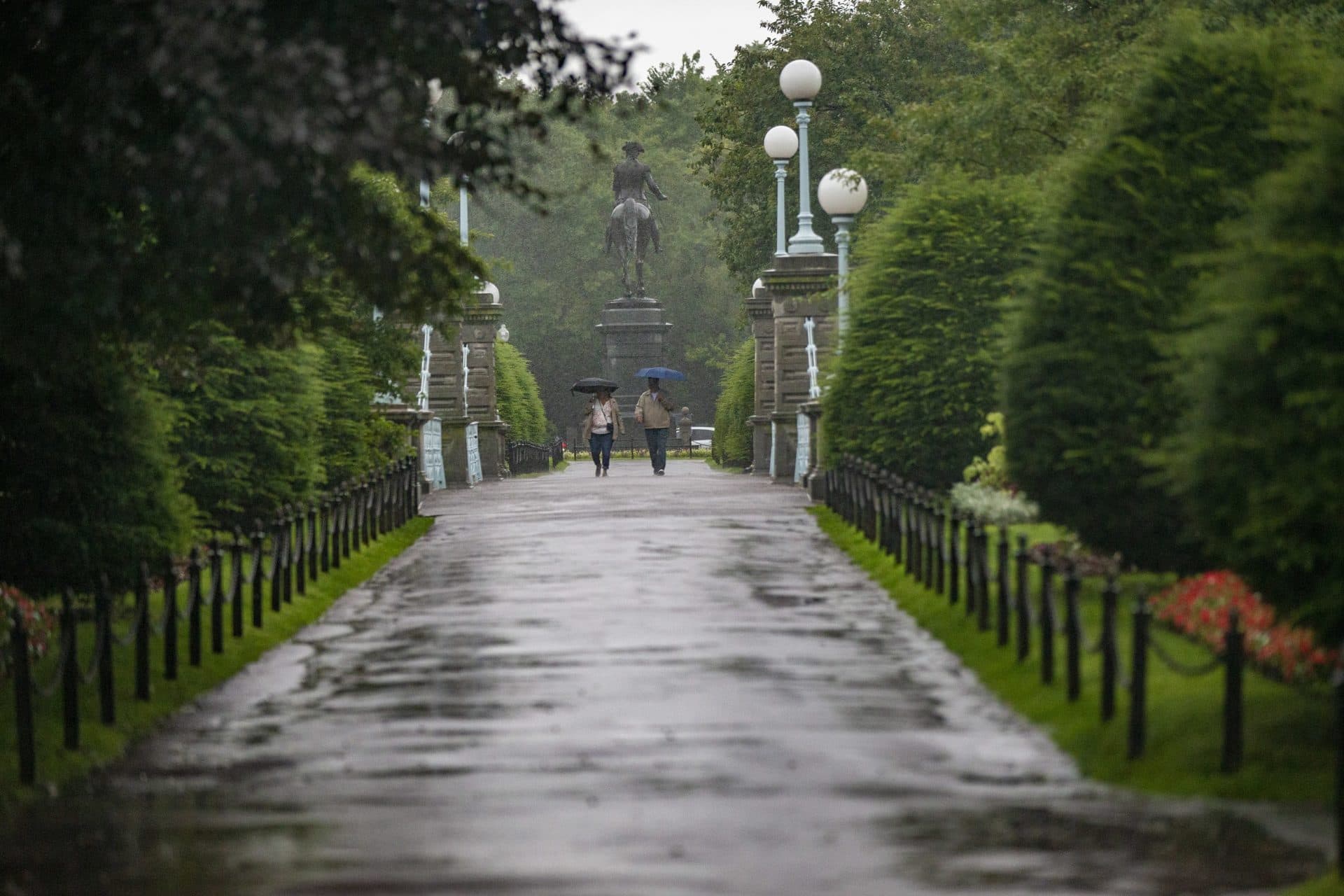 Two people with umbrellas walk over the bridge in the Boston Public Garden as Tropical Storm Elsa arrives in the area. (Jesse Costa/WBUR)