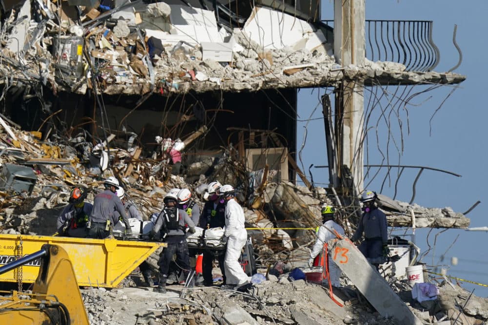 Search and rescue personnel remove remains on a stretcher as they work atop the rubble at the Champlain Towers South condo building where scores of people remain missing more than a week after it partially collapsed, Friday, July 2, 2021, in Surfside, Fla. Rescue efforts resumed Thursday evening after being halted for most of the day over concerns about the stability of the remaining structure. (AP Photo/Mark Humphrey)