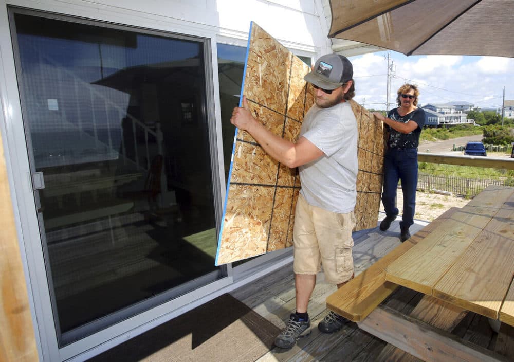 James Masog, center, and Gary Tavares, right, move particle board into place to board up the sliding glass doors of a clients house in Charlestown, R.I., ahead of Hurricane Henri, Saturday, Aug. 21, 2021. New Englanders, bracing for their first direct hit by a hurricane in 30 years, are taking precautions as Tropical Storm Henri barrels toward the southern New England coast. (Stew Milne/AP)
