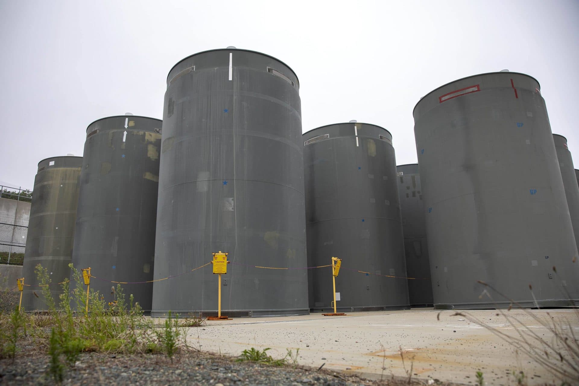 Casks containing spent fuel stand on a concrete pad near the reactor building. (Robin Lubbock/WBUR)