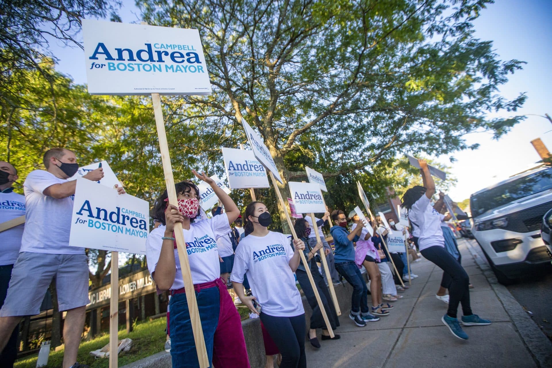 A large crowd of supporters gathers with signs outside of the Lower Mills branch of the Boston Public Library on Tuesday morning. (Jesse Costa/WBUR)