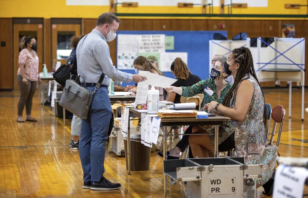A voter receives a ballot at the East Boston High School polling station. (Robin Lubbock/WBUR)